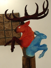 A statue of deer busts leaping from a central totem pole. The male deer has large antlers and has red fur while the female deer is sky blue.