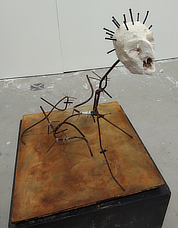 An unusual sculpture of a decapitated screaming white blocky head with nails in its skull with a spine and legs made of twisted wire.