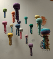 A small swarm of hand-stiched jellyfish hanging from the ceiling from different heights.