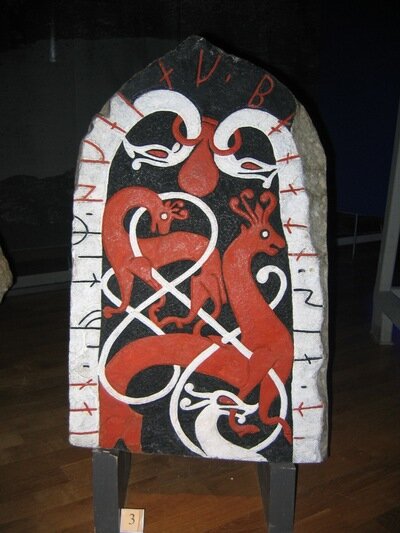 A runestone featuring dragons snakes in white with runes on them and dragons encircled within them